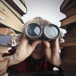 A man observing through binoculars surrounded by stacks of vintage books indoors.
