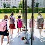 Five girls with backpacks walking into school on a sunny day.